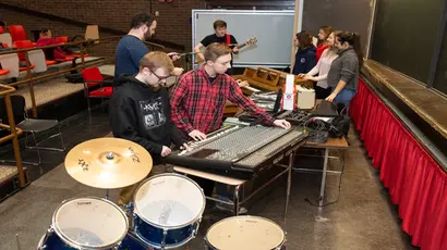 Fredonia students with musical instruments and a large, audio mixing board 