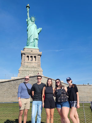 students and faculty members standing in front of the Statue of Liberty