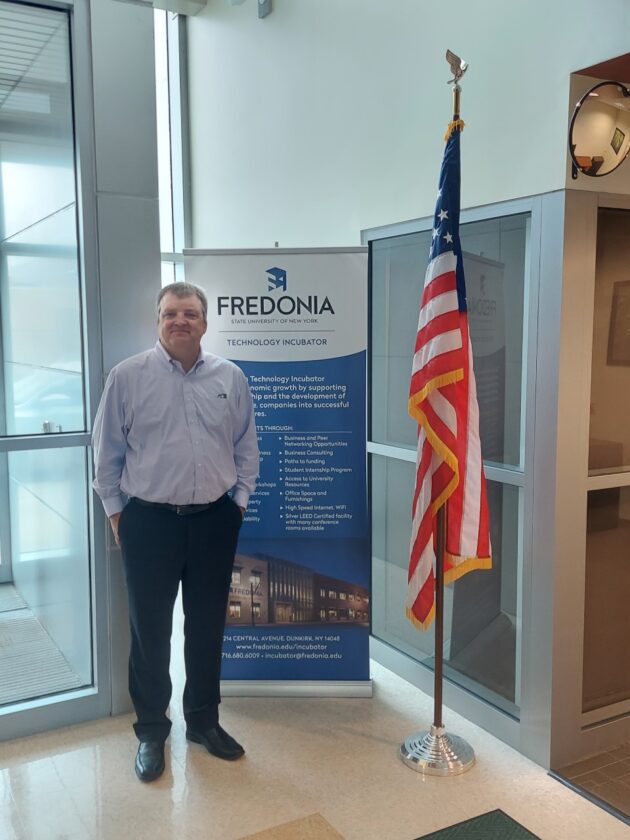 Chuck Cornell standing in front of a sign for the FTI, in the building's lobby