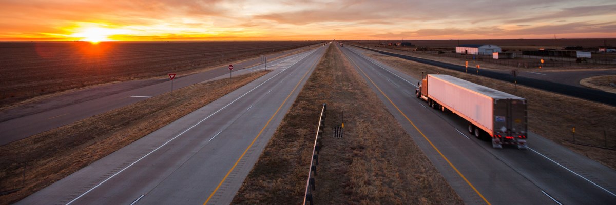 Semi truck driving on highway with sunset