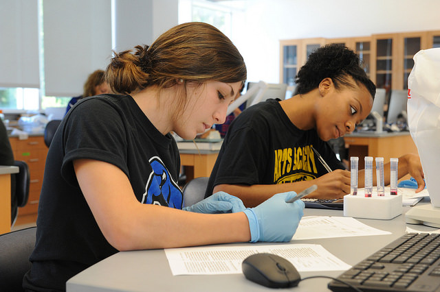 Two students take notes while conducting lab work