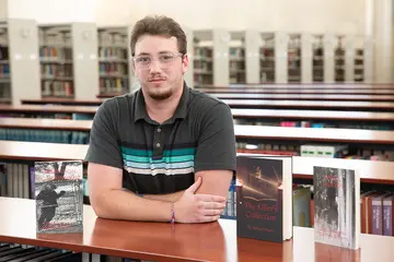 Zachary Ayers, with his three self-published books, in Reed Library.