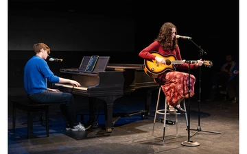 student at piano and another seated playing the guitar