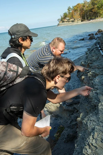 Geology majors Nicky Flores (left) and Shaun Sanders (bottom) trace a fossil-rich layer of shale with Dr. Thomas Hegna in rocks along the Lake Erie shoreline.