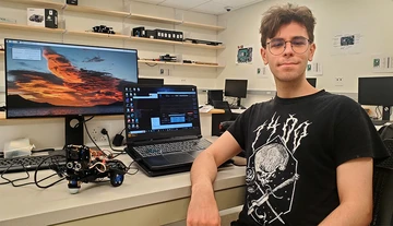 Hilmi Deniz Biliciler, with the robocar placed in front of a computer monitor to his right.