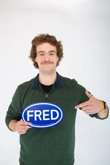Dominik Zimmer, an environmental science student in STEM holding a FRED sign 