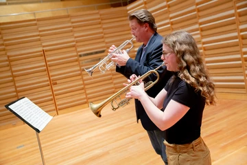 student playing trumpet alongside professor