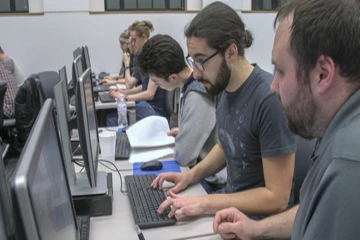 3 students examine a computer screen in the computer lab in Fenton Hall