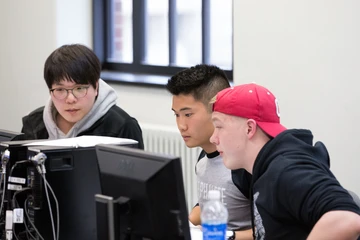 3 students examine a computer screen in the computer lab in Fenton Hall