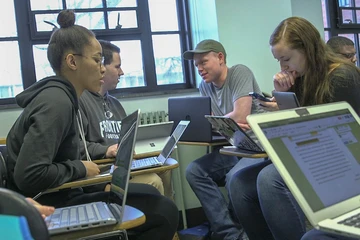 4 students sit in a cirlce in a classroom working on a project 