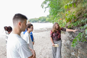 a geology professor examines a rock formation with geology students along a beach