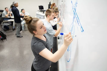 students drawing logos on a whiteboard in the front of a classroom, a degree in marketing, marketing degree, degree in marketing,  bachelor in marketing, marketing bachelor degree, jobs in marketing, business marketing.