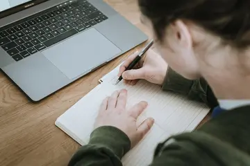 student working on a laptop. ms in graduate teaching english second language, major in graduate teaching english second language, degree in graduate teaching english second language, graduate teaching english second language major, person writing in notebook with laptop open