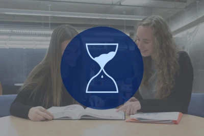 Two students work on project together in the classroom with an icon of an hourglass.