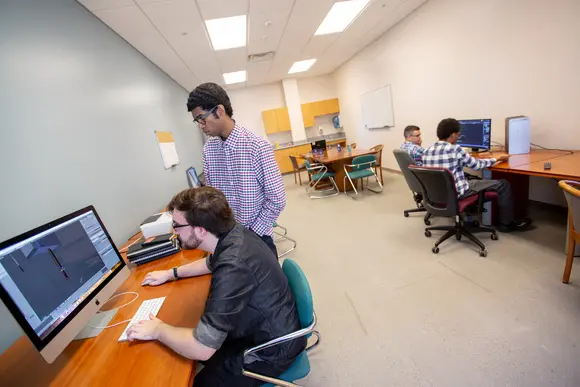 Students stand over a computer in the Center for Innovation & Economic Development (CIED)