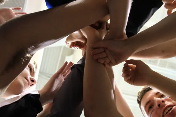 looking up from the floor at a huddle of athletes with their hands in for a cheer