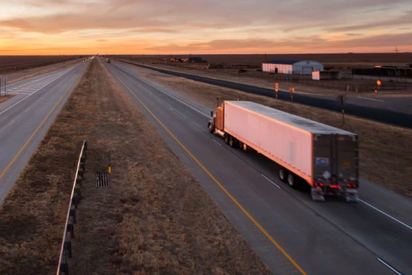Semi truck driving down highway towards sunset