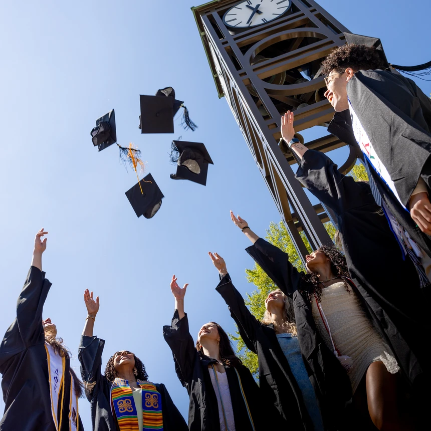 Graduates tossing their mortar boards into the air under the clock tower. 