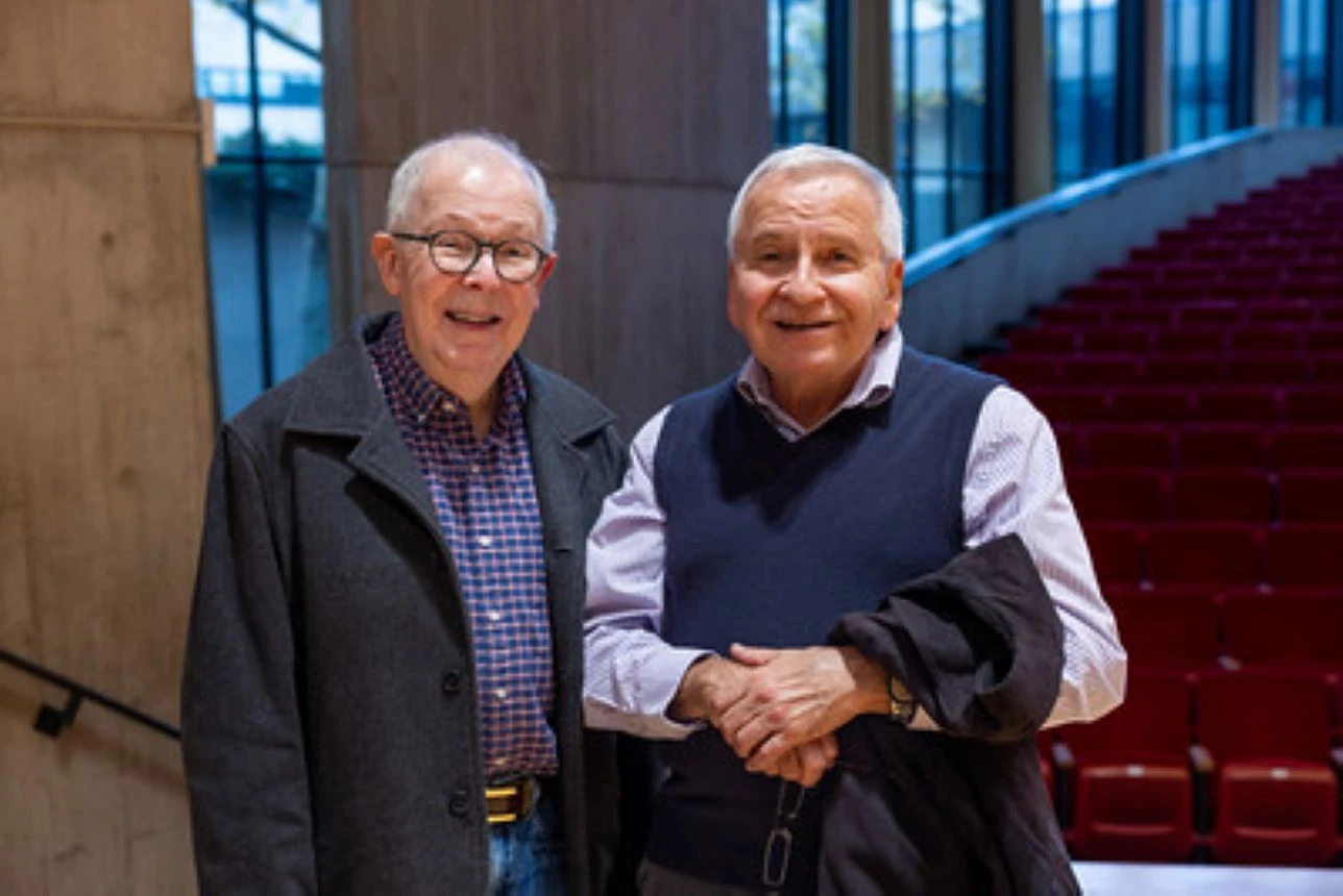 Two men pose in front of red theater seats