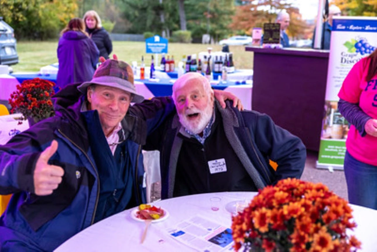 Two men at a table with wine bottles in background