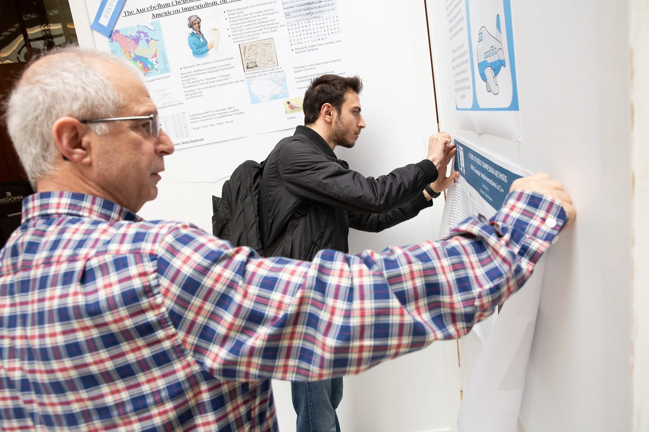 Student and professor hang research poster at OSCAR 2019.