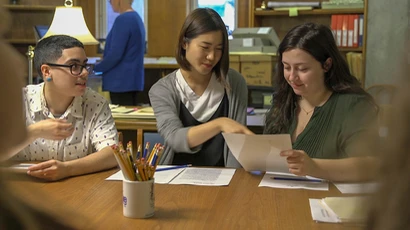 Three liberal arts students discuss a paper in class, college liberal arts