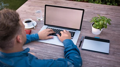 a man works on a laptop computer with a cup of coffee next to him