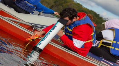 A major in biology degree student looks through a large microscope to examine underwater elements while in a canoe. biology bachelors degree