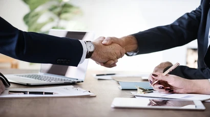 Two people engaged in a business deal shake hands across a table; business management; business manager; MBA degrees; , business managment