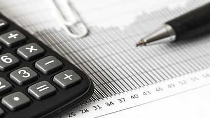 a closeup of a desk with a calculator, spreadsheets, and a pen in the foreground, CPA degree, certified public accountant degree, bachelors degree public accountancy, accounting public