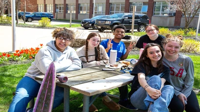 students pose for photo at picnic table on campus