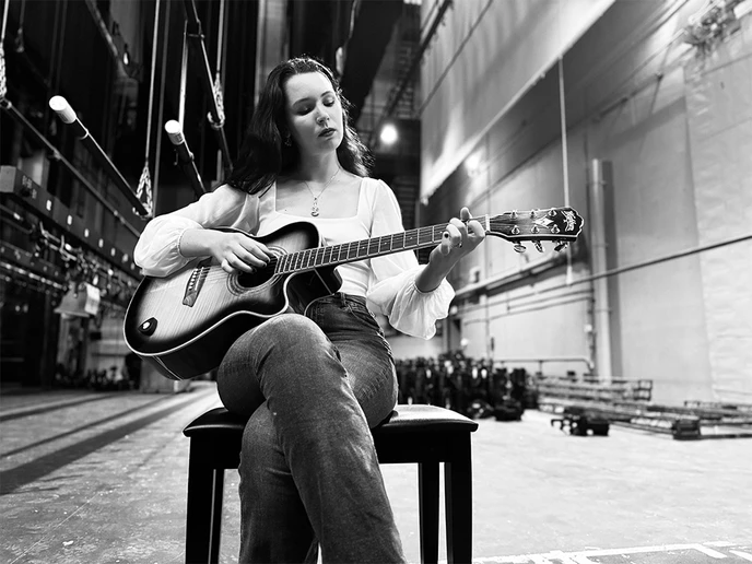 student seated and playing a guitar