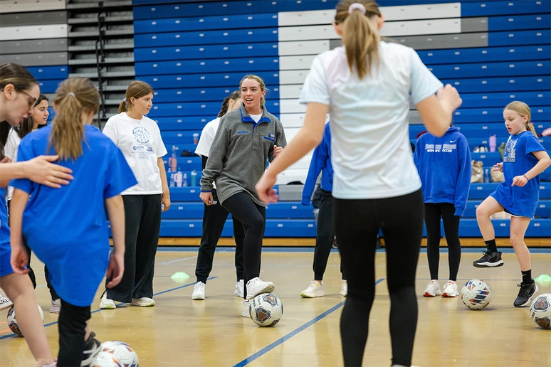 women and girls kicking soccer balls in gymnasium