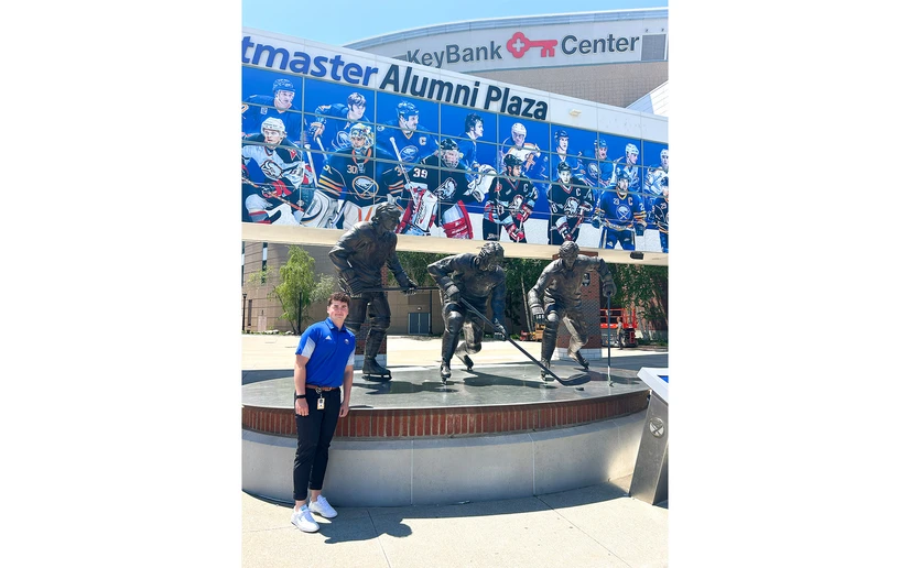 Connor West outside standing next to hockey player statues