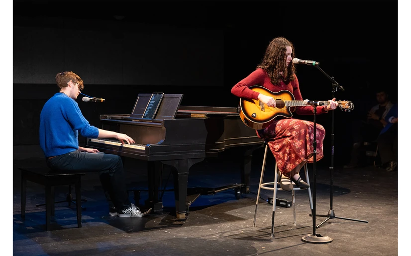 student at piano and another seated playing the guitar