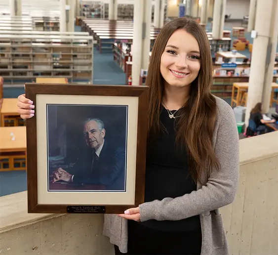 Patience Glatt, with a portrait of the late SUNY Fredonia President Emeritus Oscar E. Lanford.