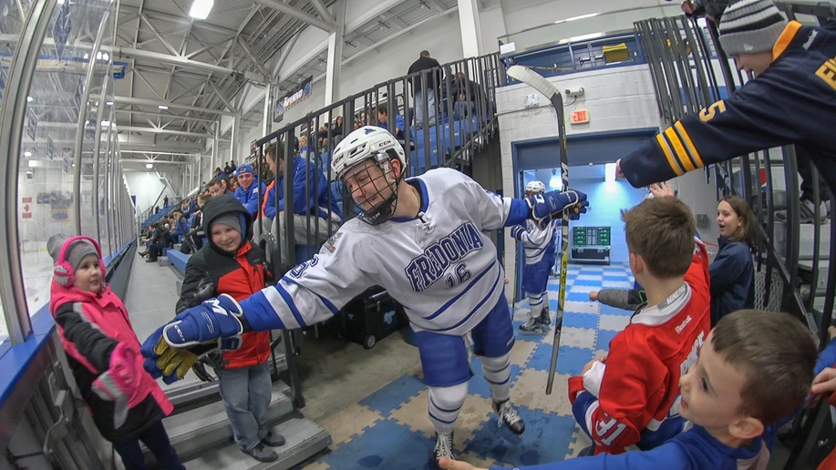 Fredonia hockey player high fiving a young fan