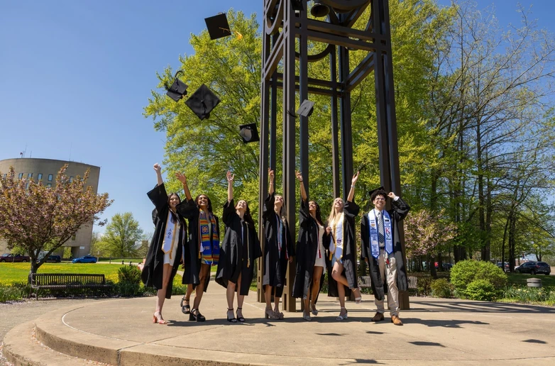 graduates throwing their mortar boards in the air under the clock tower at Fredonia