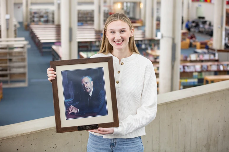 Julia T. Skiba, displaying a painting of President Emeritus Oscar E. Lanford.