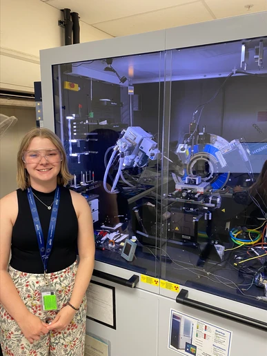 Mia Enders, in front of the micro-XRD (x-ray diffractometer) that is used to examine the diffraction patterns of crystals that that are loaded into it.
