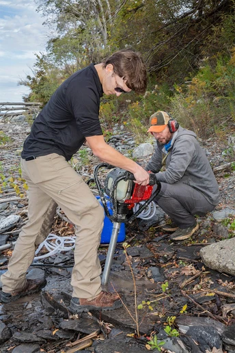 Shaun Saunders operates a drill, while Randy Blood operates a pump that injects water into the hole to cool the drill bit and wash out any rock debris generated by the bit.