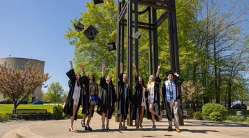 graduates throwing their mortar boards in the air under the clock tower at Fredonia