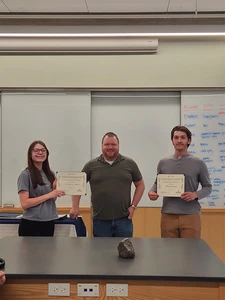 two students with certificates standing with faculty member