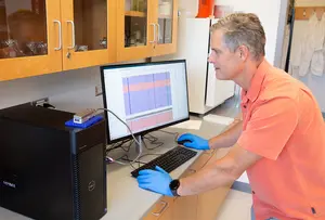The Oxford Nanopore MinION sequencer sits on top of the desktop computer, while Dr. Scott Ferguson pulls up data on the monitor.