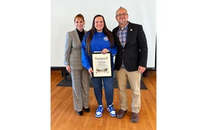 photo of Karalus holding certificate with administrators on each side