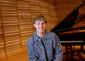 Lucas West next to the piano on stage in Rosch Recital Hall