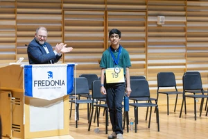 Adhrit Chowdhury receives his medallion and is congratulated by Emcee Joe Dan Harper.