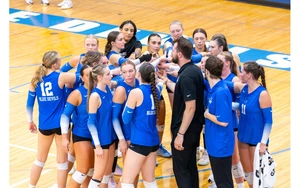 volleyball players in a huddle with coach by Travis Bernhard