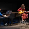 student at piano and another seated playing the guitar