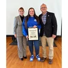 photo of Karalus holding certificate with administrators on each side